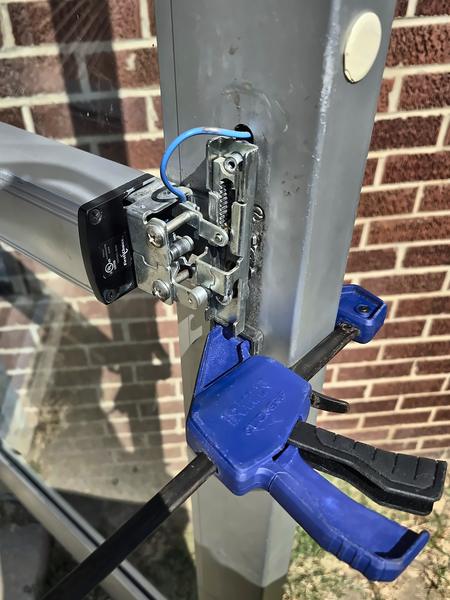 Aluminum door stile clamped with a blue bar clamp while lock hardware inside the stile is serviced