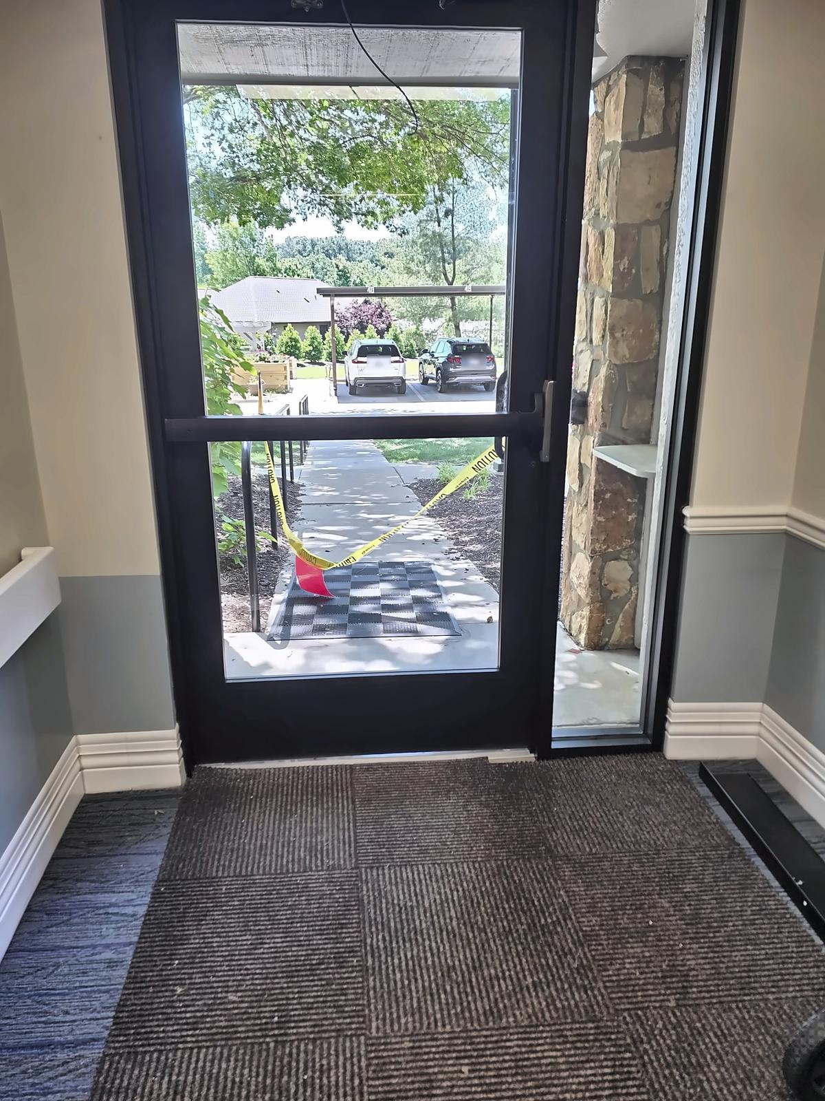 Interior view of a new dark-bronze aluminum storefront entrance door with full glass and sidelite, looking out to a walkway