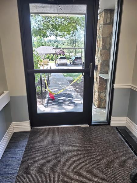 Interior view of a new dark-bronze aluminum storefront entrance door with full glass and sidelite, looking out to a walkway