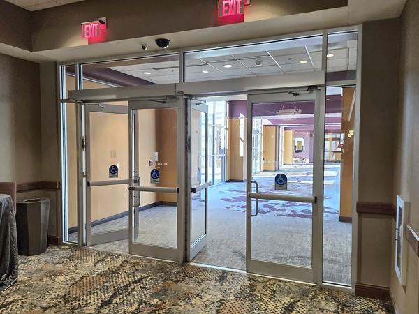 Hotel vestibule with aluminum-and-glass entrance doors under exit signs, leading into a carpeted corridor