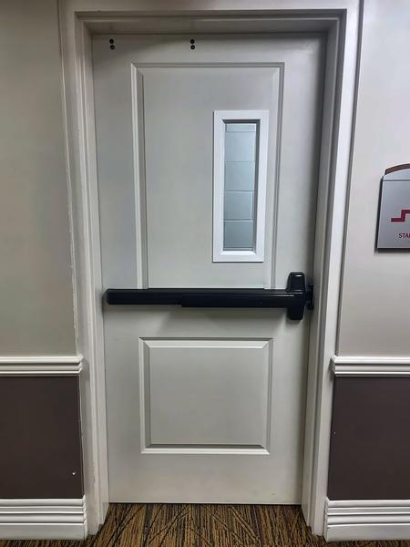 White stairwell fire door with a black panic exit bar and narrow vision window, with a stair sign on the wall