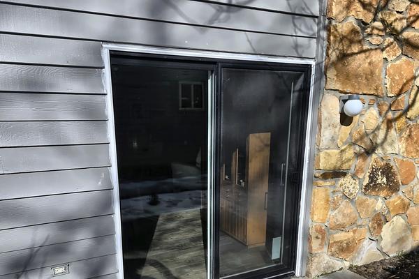 New black-framed patio sliding door installed in gray siding next to a stone wall